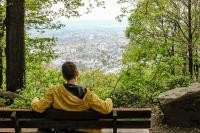 Der Heidelberger Wald ist ein Ort zum genießen und entspannen (Foto: Stadt Heidelberg/ Pellner) Ein Mann mit gelber Jacke sitzt auf einer Bank im Wald und genießt die Aussicht auf die Stadt (Foto: Stadt Heidelberg/ Pellner)