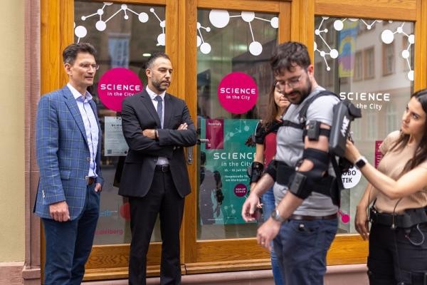 Marc Massoth (l.), Leiter des Amtes für Wirtschaftsförderung und Wissenschaft, und Prof. Dr. Lorenzo Masia (2. v. l.) schauen sich die sogenannten Exosuits in Aktion an. (Foto: Dittmer) Marc Massoth, Leiter des Amtes für Wirtschaftsförderung und Wissenschaft, und Prof. Dr. Lorenzo Masia schauen sich die sogenannten Exosuits an.