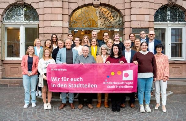 Heidelberger Kinderbeauftragte (Foto: Felix Bäcker) Gruppe der Kinderbeauftragten vor dem Rathaus. Die vorderen Personen halten ein Transparent mit der Aufschrift: Wir für euch in den Stadtteilen.