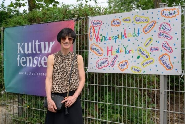 Bürgermeisterin Stefanie Jansen besuchte am 31. Juli die Kinderspielstadt Heidel York, die vom Kulturfenster e.V. in diesem Jahr an der Graf von Galen-Schule angeboten wird. (Foto: Philipp Rothe) Stefanie Jansen vor dem Kulturfensterplakat