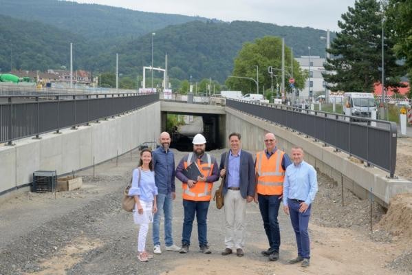 Der sogenannte Unterflieger (hinten im Bild) führt künftig unter der Montpellierbrücke entlang und wird die angrenzenden Straßen entlasten. Erster Bürgermeister Jürgen Odszuck (3.v.r.) besuchte mit Marcus Kusche (von rechts), Klaus-Peter Hofbauer und Jonas Hoffmann vom Tiefbauamt sowie Christian Hemkendreis (DSK, 2.v.l.) und Kerstin Maixner (Geschäftsstelle Bahnstadt) die Baustelle. Sechs Personen vor einer Brückenbaustelle