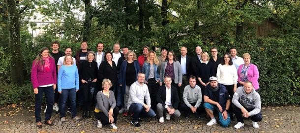 Elf Unternehmen und Institutionen machen sich auf den Weg zu einer nachhaltigen Unternehmensführung. (Foto: Stadt Heidelberg) 20 Menschen posieren für ein Gruppenfoto vor grünen Bäumen.