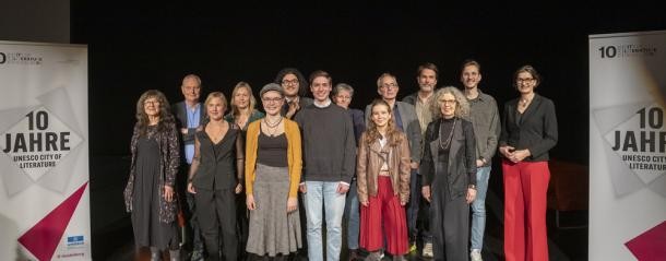 Freuen sich über die vielseitigen Rückmeldungen zum Wettbewerb „Eine Stadt schreibt“: (von links) Kuratorin Molli Hiesinger, Manfred Metzner (Jury), Nicoletta Rapetti, Claudia Kiefer (Jury), Anne Fritz (2. Preis), Derwish Seydo (Jury), Paul Liedvogel (1. Preis), Regina Wehrle (Jury), Sarah Zeiss, Karl-Heinz Grosser (3. Preis), Dirk Buff, Birgit Kreß, Marcel Kückelhaus und Kulturdezernentin Martina Pfister. (Foto: Buck) 15 Menschen stehen eingerahmt von Roll-ups auf einer Bühne.