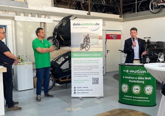 Die e-motion e-Bike-Welt war gastgebendes Unternehmen beim Afterwork-Event des Bundes Wieblinger Selbstständiger. (Foto: Stadt Heidelberg) Man sieht einen Redner und zwei zuhörende Männer beim Afterwork-Event.