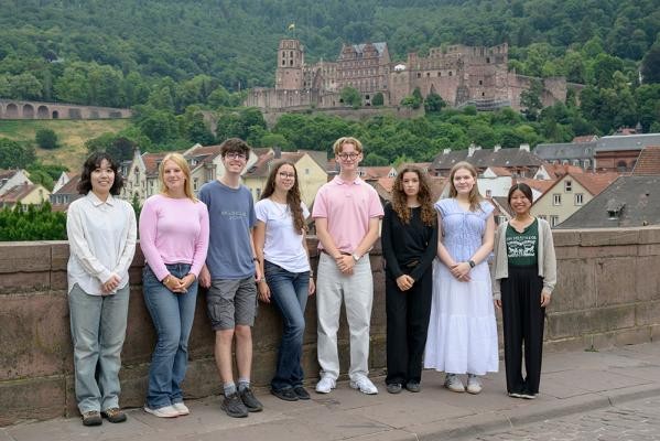 Die Teilnehmerinnen und Teilnehmer der 28. International Summer Science School Heidelberg 2025 kamen am 14. Juli 2025 zu einem gemeinsamen Foto auf der Alten Brücke zusammen. (Foto: Rothe) Eine Gruppe Jugendlicher posiert auf der Alten Brücke, hinter ihnen das malerische Heidelberger Schloss.