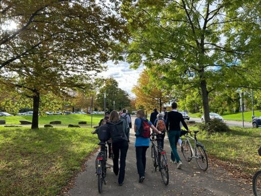 Auf der Straße Im Neuenheimer Feld (rechts) sollen künftig nur Straßenbahnen fahren, keine Autos mehr. Ein Radweg dort bleibt erhalten. (Foto: Stadt Heidelberg) Menschen spazieren einen Weg entlang.