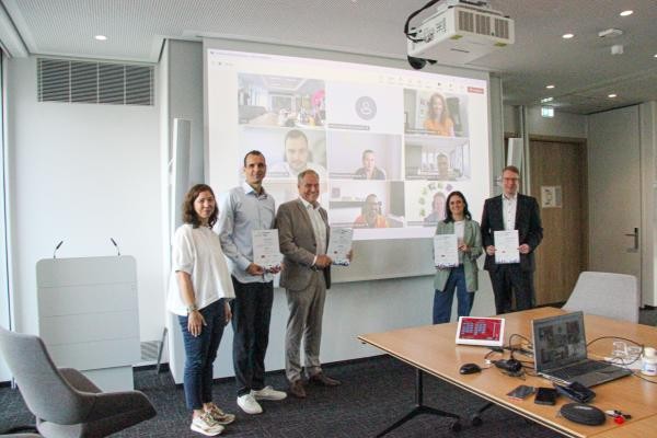 Freuten sich über den erfolgreichen Wettbewerbsauftakt bei „Test in Heidelberg“ (von links): Mareike Rimmler, Projektleiterin Team Innovation bei der Stadt Heidelberg, Sebastian Warkentin, Geschäftsführer der Digital-Agentur Heidelberg, Oberbürgermeister Eckart Würzner, Katharina Schimek-Hefft, Abteilungsleitung Marketing und Kundenservice Stadtwerke Heidelberg, und Stefan Schneider, Bereichsleiter Organisationsentwicklung Sparkasse Heidelberg. (Foto: Stadt Heidelberg) Eine Gruppe steht vor einer Leindwand