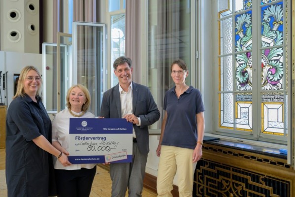 Erster Bürgermeister Jürgen Odszuck (2. v. r.) besichtigt bei seiner Baustellen-Sommertour die Arbeiten zur Fenstersanierung an der Musik- und Singschule. Dabei kann er eine Förderung über 80.000 Euro von der Deutschen Stiftung Denkmalschutz entgegennehmen, die Ortskuratorin Helen Heberer (2. v. l.) übergibt. (Foto: Philipp Rothe) Erster Bürgermeister Jürgen Odszuck nimmt vor der Fensterfront den großen Scheck von Helen Heberer entgegen.