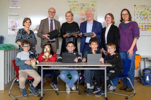 Neue iPads machen Sprachförderunterricht abwechslungsreicher (von links): Rektorin Andrea Czernoch (IGH-Primarstufe), Prof. Frieder Hepp (Rotary Club), Isabel Arendt (Amt für Schule und Bildung), Prof. Bernhard Eitel (Rotary Club), Elvira Weber (päd-aktiv e. V.) und Christina König (päd-aktiv e. V.) mit Kindern des Sprachförderunterrichts bei der Spendenübergabe an der IGH-Primarstufe. (Foto: Philipp Rothe) Abgebildet sind 5 Kinder die mit Plüschtieren oder Ipads hinter einem Tisch sitzen. Hinter ihnen stehen aufgereiht 6 Erwachsene .