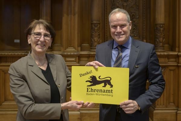 Oberbürgermeister Eckart Würzner und Dr. Ute Leidig, Staatssekretärin im baden-württembergischen Ministerium für Soziales, Gesundheit und Integration, haben die ersten Ehrenamtskarten in Heidel-berg an Ehrenamtliche ausgegeben und die Landesehrenamtskarte vorgestellt. Zwei Personen halten eine große Ehrenamtskarte in der Hand.