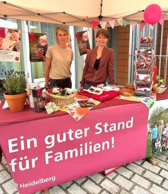 Yvonne Spiller (links) und Natalia Stein sind mit dem Familienbüro wieder on Tour: am 25. März 2026 bei der Familienkasse Baden-Württemberg West am Czernyring 22/11. (Foto: Stadt Heidelberg) Zwei Frauen, die hinter dem Stand des Familienbüros stehen.