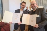 Die Badische Peptide und Proteine GmbH bekam den Innovationspreis Bioökonomie samt Publikumspreis verliehen. (Foto: BPP) Zwei Männer lächeln in die Kamera, sie halten beide jeweils eine Urkunde in den Händen.