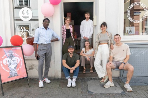 Präsentieren im neuen Konzeptladen HeartWork ihre Produkte (von links): Madiagne Diop, Lena Grunder, Oliver Matlock, Simon Fritz, Alexandra Quandt, Sofia Leser und Moritz Stock. (Foto: Larionova) Mehrere Menschen sitzen, stehen und hocken vor einem Laden, der mit pastellfarbeenen Luftballons geschmückt ist.