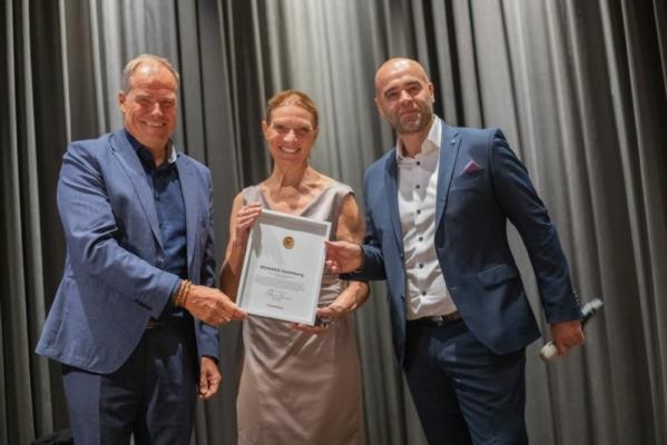 Oberbürgermeister Eckart Würzner überreichte den beiden Geschäftsführern von Rehamed Heidelberg Susanne Jung-Fromm und Karlos Yacoub das Heidelberger Wirtschaftssiegel (v.l.). (Foto: Rehamed) Drei Personen stehen mit einer Urkunde vor einem grauen Vorhang.