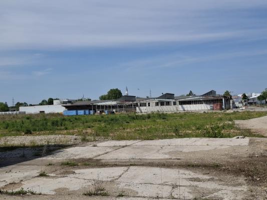 Leerstehende und versiegelte Flächen im interkommunalen Gewerbegebiet Heidelberg-Leimen sollen bald entwickelt werden – mithilfe einer weiteren Landesförderung. (Foto: Zweckverband „Interkommunales Gewerbe- und Industriegebiet Heidelberg-Leimen“) Zu sehen ist ein Schnappschuss des Industriegebiets. Im Hintergrund sind mehrere Gebäude zu sehen und im Vordergrund sieht man eine Betonfläche und eine mit Pflanzen und Gras überwachsene Fläche.