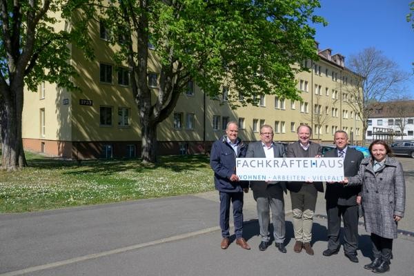 Die Eröffnung des Fachkräftehauses in der Römerstraße. (Foto: Rothe) Vier Männer und eine Frau stehen vor einem Gebäude. Sie halten ein Schild in den Händen, auf dem "Fachkräftehaus" steht.