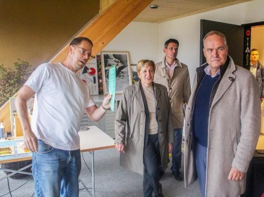 Landesministerin Nicole Razavi besuchte den hip und bekam eine Führung von Oberbürgermeister Eckart Würzner (r.). (Foto: Stadt Heidelberg) Drei Männer und eine Frau stehen in einem Büroraum. Der Eine Mann zeigt auf etwas, wo die anderen hinschauen.