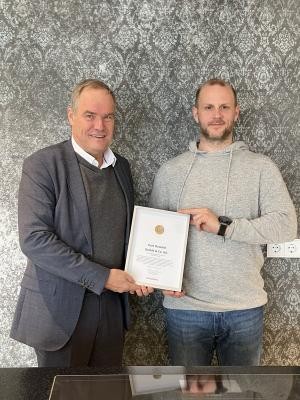 Oberbürgermeister Eckart Würzner überreicht das Wirtschaftssiegel an Geschäftsführer Thomas Oswald. (Foto: Stadt Heidelberg) Zwei Männer schauen in die Kamera. Der eine übergibt eine Urkunde mit Siegel in einem Rahmen an den anderen.