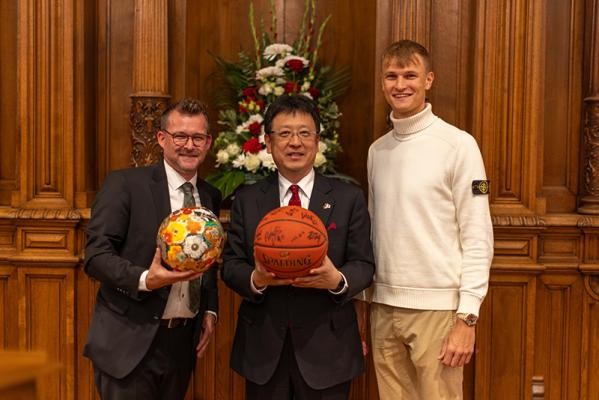 Heidelberg und Kumamoto planen regelmäßige Austausche im Jugendsport, beginnend vor allem im Fußball und Basketball. Kumamotos Oberbürgermeister Kazufumi Onishi (Mitte) überreichte Bürgermeister Raoul Schmidt-Lamontain (links) symbolisch einen verzierten Fußball. Im Gegenzug schenkte Niklas Würzner, Spieler des Basketball-Bundesligisten MLP Academics Heidelberg, den Gästen aus Kumamoto einen von den Spielern unterschriebenen Basketball. (Foto: Tobias Dittmer) Heidelberg und Kumamoto planen regelmäßige Austausche im Jugendsport, beginnend vor allem im Fußball und Basketball. Kumamotos Oberbürgermeister Kazufumi Onishi (Mitte) überreichte Bürgermeister Raoul Schmidt-Lamontain (links) symbolisch einen verzierten Fußball. Im Gegenzug schenkte Niklas Würzner, Spieler des Basketball-Bundesligisten MLP Academics Heidelberg, den Gästen aus Kumamoto einen von den Spielern unterschriebenen Basketball. (Foto: Tobias Dittmer)