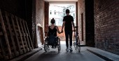 Eine junge Frau im Rollstuhl und ein junger Mann mit einem Fahrrad halten Hände. Der Mann schiebt ein Fahrrad (Foto: Weiland)