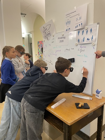 Kinder stehen vor einer Tafel und testen mit den Brillen zu schreiben