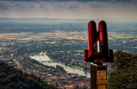 Im Vordergrund ein rotes Fernglas, im Hintergrund Heidelberg und der Neckar von oben.