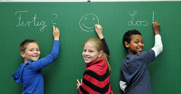 Drei Kinder stehen vor einer Tafel und schreiben und malen darauf.