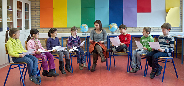 Lehrerin mit Kindern im Stuhl-Halbkreis beim Lesen